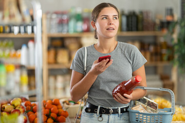 Fototapeta premium Female shopper scanning QR code on bottle tomato juice label in grocery department of supermarket