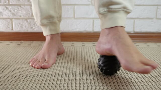 Myofascial foot release with a massage ball. Close-up view of a man's bare feet rolling on a spiky massage ball for self-massage, helping to relieve plantar fasciitis pain and improve circulation