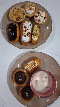 A Selection of Eclairs Arranged on Plates, Viewed from Above. Vertical Video of Delicious Pastries with Various Toppings and Flavors