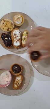 Selection of Eclairs Arranged on Plates, Viewed from Above. Vertical Video of Delicious Pastries with Various Toppings and Flavors