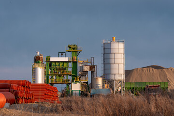 Obraz premium An asphalt plant with silos, machinery, and construction materials under clear sky in industrial setting