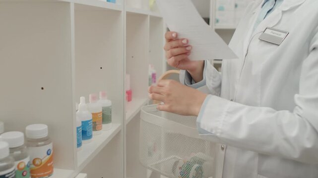 Side view detail shot of young Caucasian woman as pharmacist preparing order for customer taking medications off shelves and putting into basket in storage room, copy space