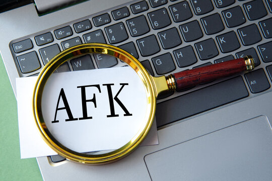 AFK - acronym on a white sheet under a magnifying glass next to a laptop