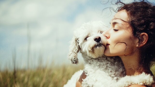 Romantic love theme for Valentines Day. A woman tenderly embracing a white dog in a field, with a blurred background suggesting a shallow depth of field.