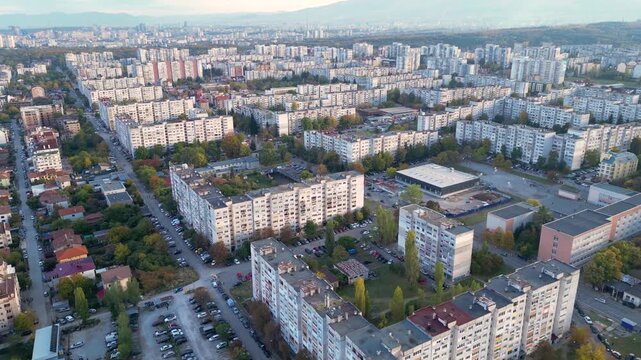 Drone aerial panorama of a densely populated residential district in Sofia, Bulgaria featuring apartment buildings, city streets, parks, and the skyline with Vitosha Mountain in the background. Wide e