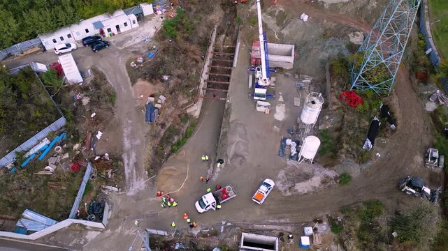Vertical aerial drone footage of an active construction site where a drilling rig and construction crew perform foundation and ground engineering work. The scene highlights excavation, heavy machinery