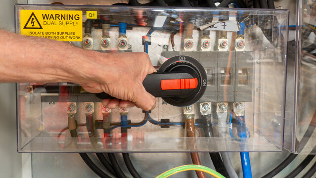 Specialist electrical test and commissioning engineer activating a power breaker on an automatic transfer switch. Emergency systen back up generator for electrical power.