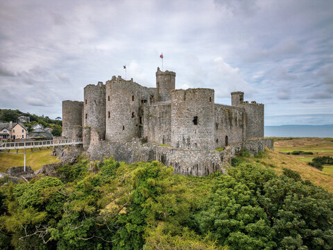 Aerial view of Castell Harlech, a medieval stone fortress with massive round towers on a rocky outcrop surrounded by lush green trees Harlech, Wales, United Kingdom.