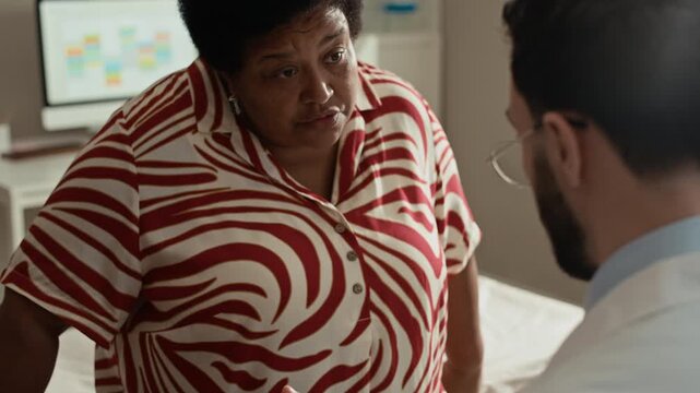 Tilt up over shoulder shot of senior Black female patient asking questions while doctor demonstrating insulin injection pen during diabetes appointment