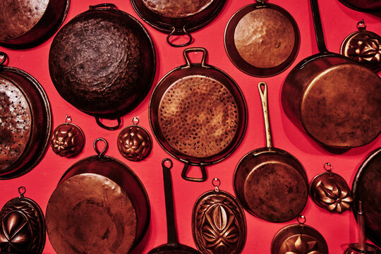antique copper kitchen pots, pans, and molds arranged against a solid background
