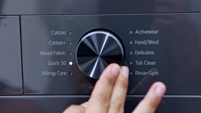 Hand turning the program selector dial on a modern washing machine