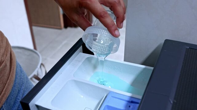 Person pouring liquid laundry detergent into washing machine drawer