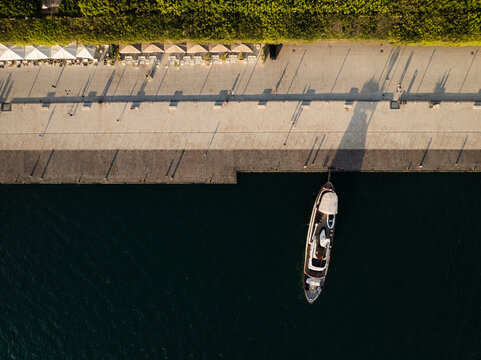 Aerial view of the Island of Ortigia waterfront with a docked boat and long shadows on the promenade in Syracuse, Sicily, Italy.