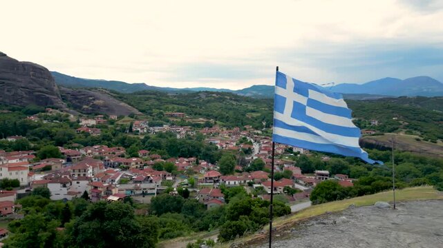 Epic Torn Greek Flag Aerial Drone Blowing in Wind Close Up. Move Around it With Village and Mountains in the Background in Meteora, Greece