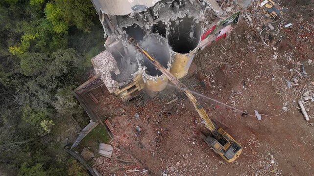 Aerial drone footage of a partially demolished industrial building featuring large concrete silos, collapsed masonry walls, and piles of construction debris. The scene documents urban redevelopment, i