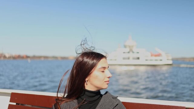 Long haired brunette girl sitting on ship deck while large vessel passes in background calm sea travel atmosphere coastal tourism freedom lifestyle cinematic outdoor scene