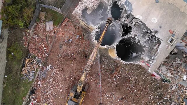 Aerial drone footage of a partially demolished industrial building featuring large concrete silos, collapsed masonry walls, and piles of construction debris. The scene documents urban redevelopment, i