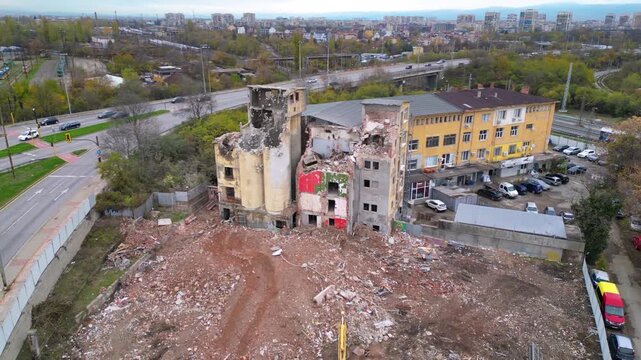 Aerial drone footage of a partially demolished industrial building featuring large concrete silos, collapsed masonry walls, and piles of construction debris. The scene documents urban redevelopment, i