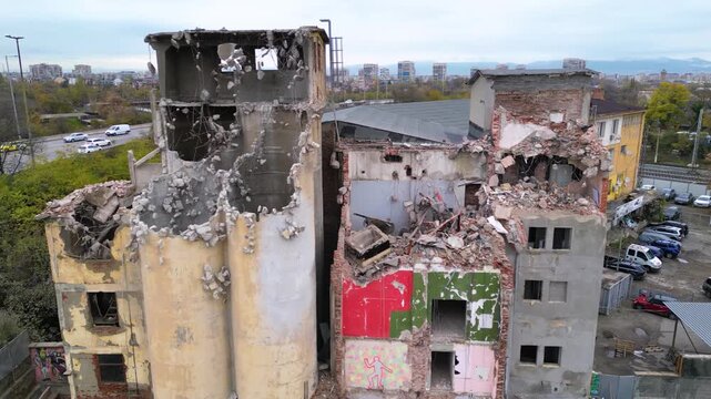 Aerial view of a partially demolished industrial building beside an active urban road, with exposed concrete structures, rubble piles and heavy damage showing an ongoing demolition and redevelopment s