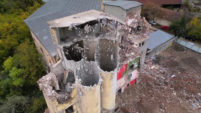 Aerial drone footage of a partially demolished industrial building featuring large concrete silos, collapsed masonry walls, and piles of construction debris. The scene documents urban redevelopment, i