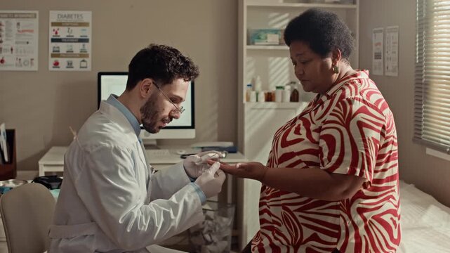 Side view medium shot of male physician testing African American senior female patient blood sugar using glucometer during diabetes management appointment in healthcare office