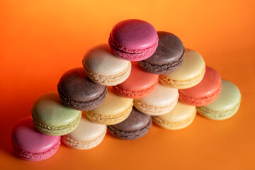 Fototapeta premium Sweet Colorful Macarons on Bright Orange Surface. Pastel Macarons Dessert Composition on Orange Backdrop. French Macarons Assorted Colors. 