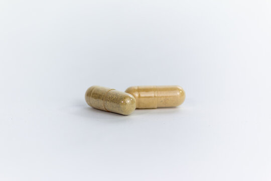 Two Herbal Medicine Capsules Filled with Natural Brown Powder Isolated on White Background