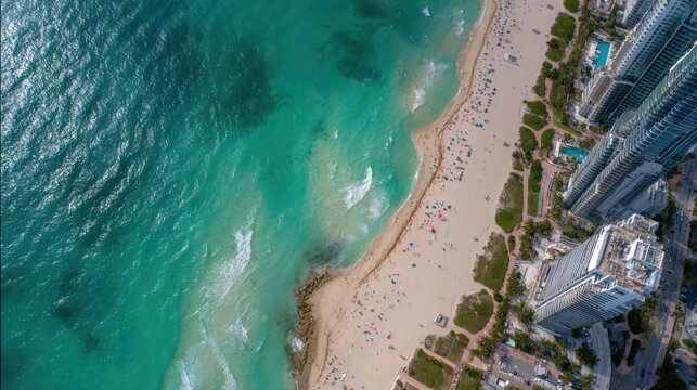 High-angle view of a vibrant beach scene, showcasing turquoise water lapping at a sandy shore lined with modern high-rise buildings.