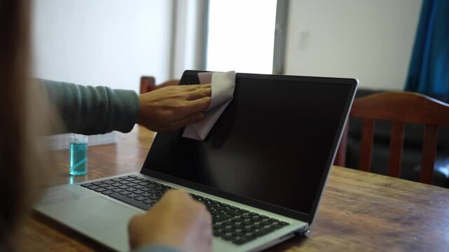 Person cleaning laptop keyboard and screen with disinfectant spray