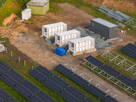Aerial view of FVE Bohumilice solar farm with rows of photovoltaic panels and white battery storage containers on a dirt field in Klobouky u Brna, Jihomoravsky kraj, Czechia.