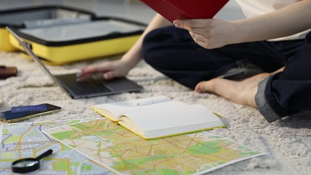Woman with passport, laptop and map planning trip on floor at home, closeup
