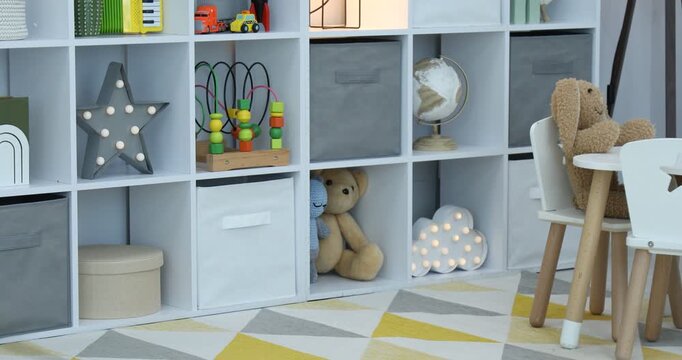 Shelving unit with different toys and decor near light grey wall in child's room. Camera moving left