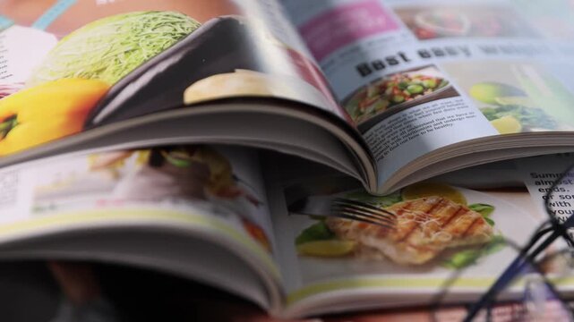 Open lifestyle magazines and glasses on wooden table, closeup. Camera moving
