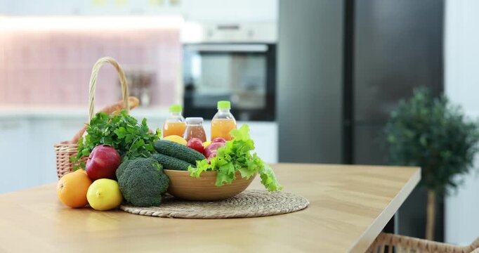 Fresh vegetables, fruits, bread and drinks on wooden table in kitchen, camera moving in