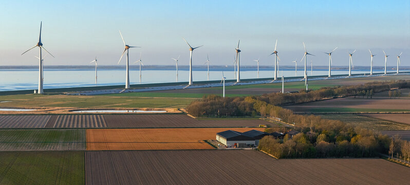 Aerial view of a row of wind turbines along a coastal dike and colorful agricultural fields Netherlands.