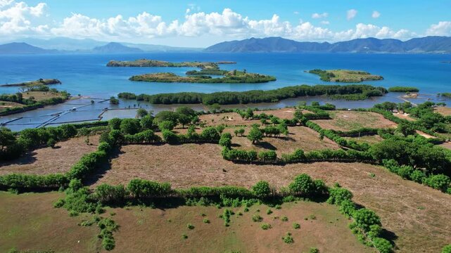 Aerial drone footage of dry hills with green bushes, with paradise small islands behind in blue sea, in Bajo village, Dompu regency, Sumbawa, Indonesia