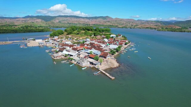 Aerial drone footage of old Bajo village, with a jetty, local wooden and metallic roof houses, fishing boats, with stunning bay behind in turquoise sea, in Dompu regency, Sumbawa island, Indonesia