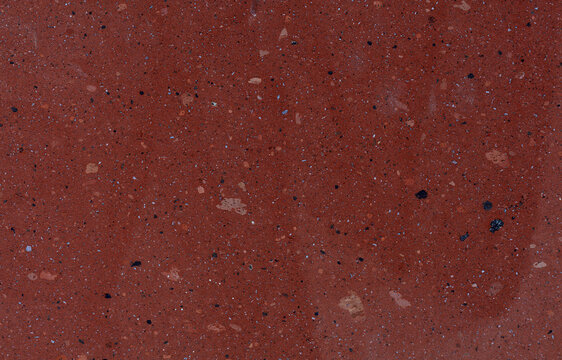 A close-up of a texture sample of red tuff facing stone interspersed with small pebbles.