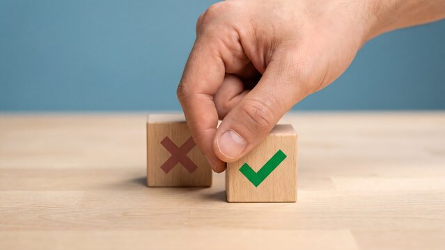 A hand places a wooden block with a green checkmark on top of another block with a red X on a wooden surface.