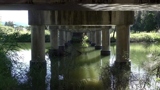 Symmetrical bridge underpass over light green river with concrete pillars framing calm water scene