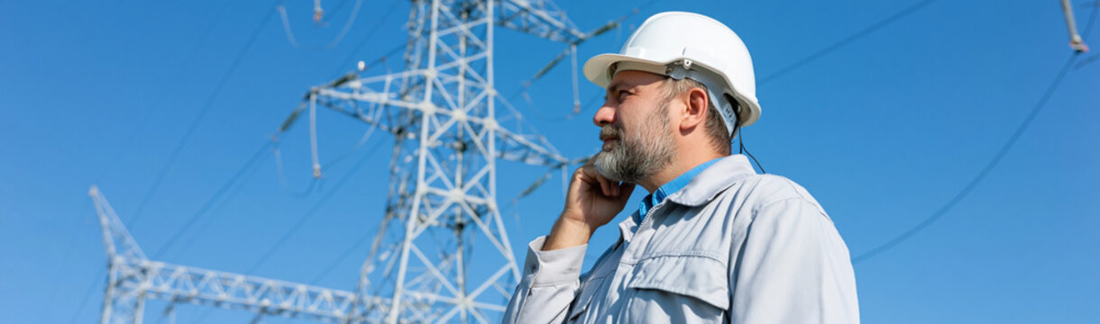 Industry Professional on Duty: A focused technician, clad in a safety helmet, engages in a crucial call near an electricity pylon, embodying diligence and expertise in their work. 