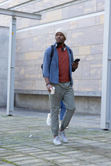 African American adult male walking in paved courtyard, wearing beanie, holding coffee cup, phone © wavebreak3