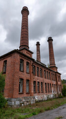 Fototapeta premium Historical Brick Factory: A striking image of a historic brick factory, its tall chimneys reaching towards a cloudy sky. The weathered facade whispers tales of a bygone industrial era.