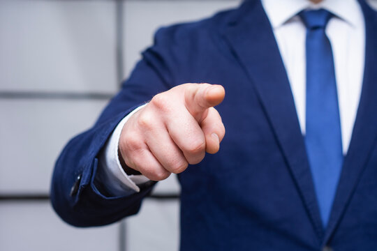 Businessman in navy suit and blue tie pointing finger toward camera. Concept for leadership, decision making, business direction, and corporate choice.
