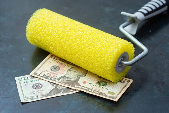 Yellow foam paint roller placed on ten and twenty dollar bills on dark background. Concept for painting service cost, renovation budget, and home improvement expense.