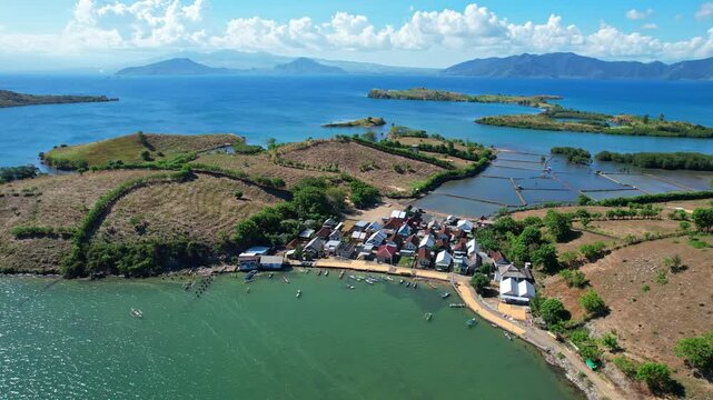 Aerial drone footage of Bajo village, with white sandy beach, local wooden and metallic roof houses, fishing boats, with stunning islands behind in blue sea, in Dompu regency, Sumbawa, Indonesia