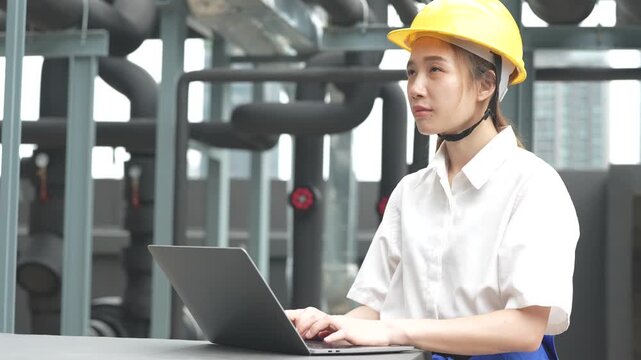 A professional female engineer wearing a yellow hardhat uses a tool to perform a technical electrical control panel audit and facility maintenance.