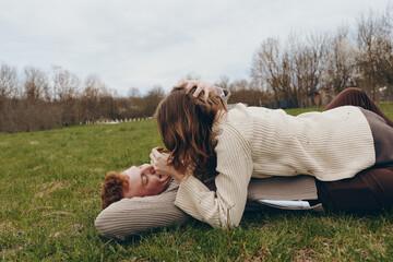 Fototapeta premium couple affection outdoors friendship laughter on the grass, a woman and a man share a playful moment in cozy sweaters, under a clear sky, showcasing casual lifestyle, outdoor leisure, and genuine