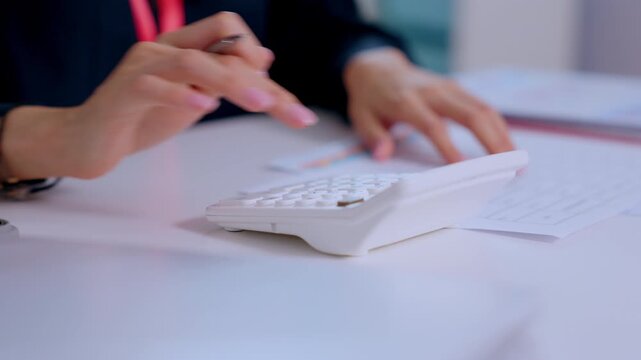 Focused professional hand pressing white calculator on office desk reviewing corporate finance document doing complex business accounting calculation and paperwork with deep concentration