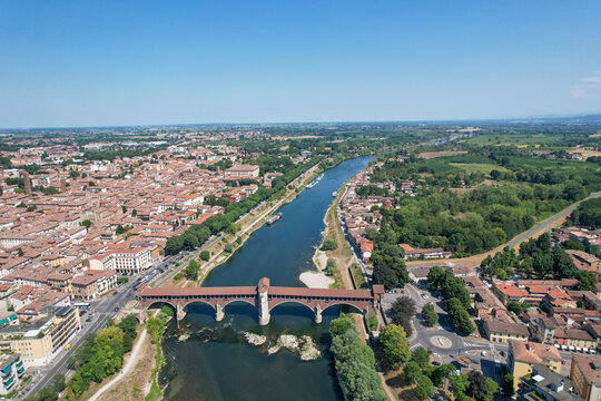 Aerial view of the historic Ponte Coperto spanning the Ticino River with the city skyline and lush greenery Pavia, Lombardy, Italy.